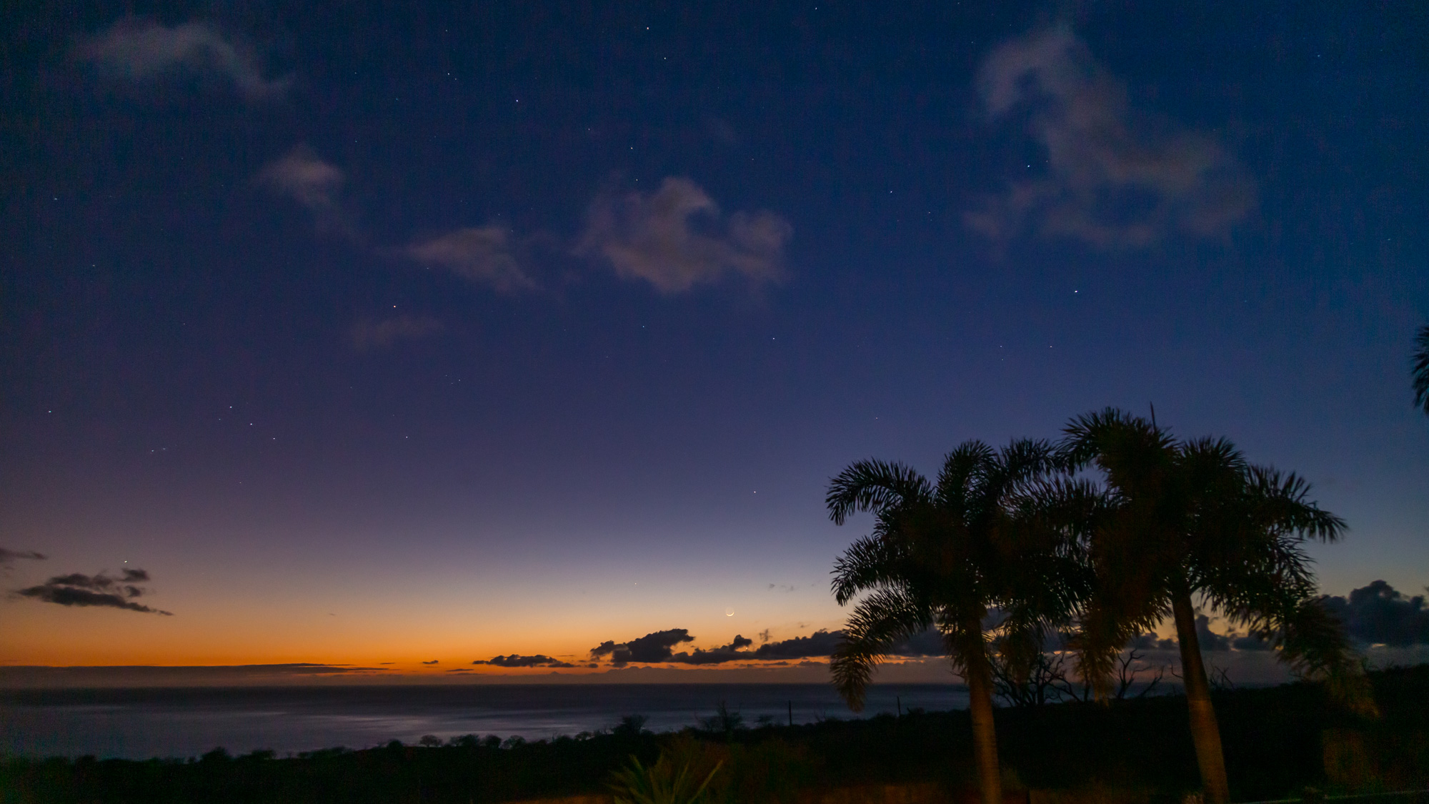 The crescent Moon setting over the Pacific ocean while Venus is visible peeking out between the clouds below the Moon.  Mercury (above and slightly to the right of the Moon) and Mars (near the top of the frame) are also visible.
